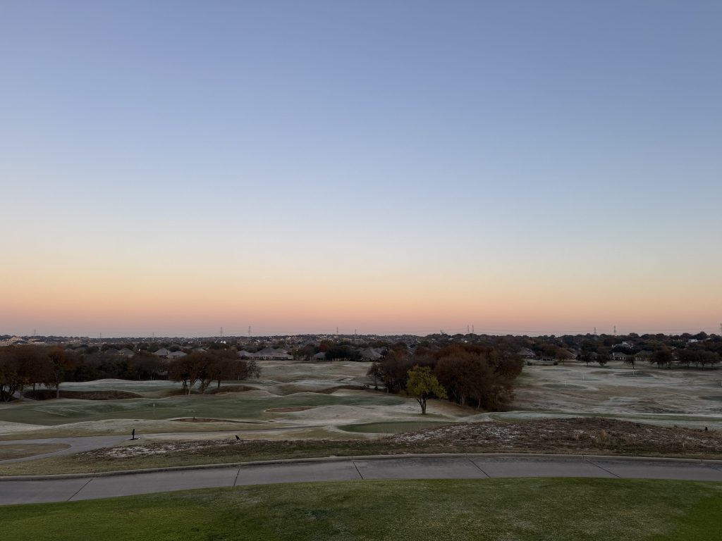 View from a cart path overlooking the course. Trees and dunes dot the landscape on an early morning.